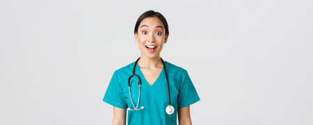 Healthcare workers, preventing virus, quarantine campaign concept. Happy and excited asian female doctor, physician in scrubs look amazed, hear awesome news, white backgroundの写真素材