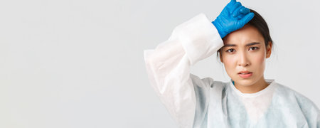 Covid-19, coronavirus disease, healthcare workers concept. Young tired asian female doctor take-off...