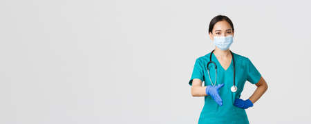 Covid-19, coronavirus disease, healthcare workers concept. Confident young asian female doctor, physician in scrubs and medical mask, gloves, extend hand for handshake, greeting patientの写真素材