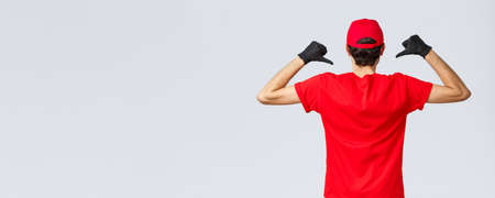 Covid-19, self-quarantine, online shopping and shipping concept. Back view of courier pointing at his t-shirt to show carrier company logo, courier promote service of delivery during coronavirusの写真素材
