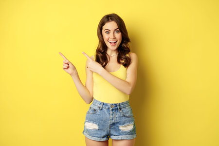 Portrait of stylish summer girl, brunette woman showing way, pointing fingers left, advertising,...