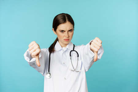 Woman doctor, medical worker showing thumbs down and frowning angry, dislikeの写真素材