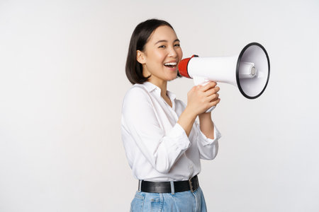 Image of young woman, korean activist, recruiter screaming in megaphone, searching, shouting at loudspeaker, standing over white backgroundの写真素材