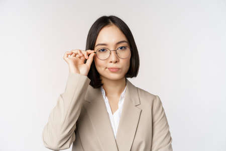Professional asian businesswoman in glasses, looking confident at camera, standing in power pose against white backgroundの写真素材