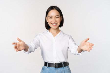 Image of smiling asian woman welcoming guests clients, businesswoman stretching out open hands, greeting, standing over white backgroundの写真素材