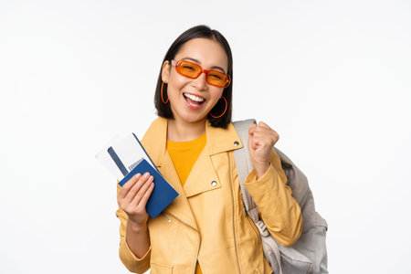 Happy asian girl going on vacation, holding passport and flight tickets, backpack on shoulder. Young woman tourist travelling abroad, standing over white backgroundの写真素材
