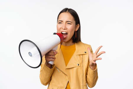 Portrait of young asian woman protester, screaming in megaphone and protesting, standing confident against white backgroundの写真素材