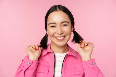 Skin care and cosmetology concept. Beautiful asian girl smiling and laughing, showing clean healthy facial skin, posing against pink backgroundの写真素材