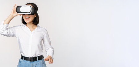 Excited young woman enter virtual reality in her glasses. Asian girl using vr headset, standing over white backgroundの写真素材