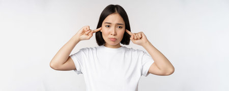 Portrait of asian woman shut ears and feeling discomfort from loud noise, annoying sound, standing...