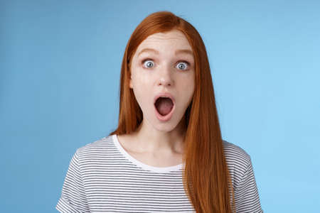 Wow so cool. Impressed speechless amused attractive redhead girl blue eyes freckles open mouth wide omg drop jaw astonished express surprise amazement, standing blue backgroundの写真素材