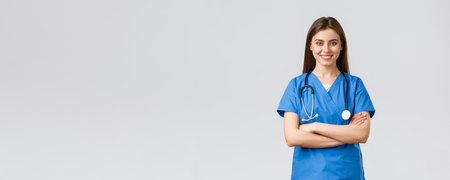Medical workers, healthcare, covid-19 and vaccination concept. Optimistic confident, professional female nurse or doctor in blue scrubs with stethoscope, cross arms chest and smiling optimisticの写真素材