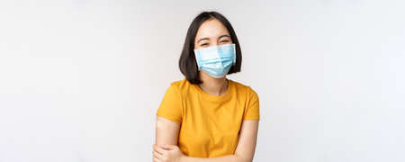 Healthy and happy asian woman in medical face mask, has bandaid on shoulder after covid-19 vaccination, got vaccinated from omicron delta variant, white backgroundの写真素材