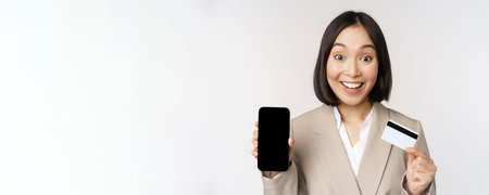 Corporate woman with happy, enthusiastic face, showing credit card and smartphone app screen,...