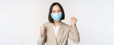 Coronavirus and business people concept. Happy businesswoman in medical face mask dancing, celebrating success, achievement, standing over white backgroundの写真素材