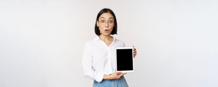 Enthusiastic asian woman, office worker in glasses showing digital tablet screen, demonstrating info...