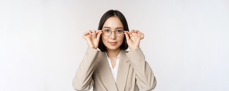 Smiling asian businesswoman trying new glasses, wearing eyewear, standing in suit over white backgroundの写真素材
