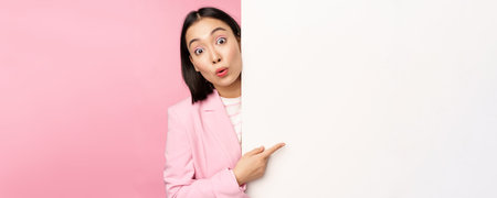 Portrait of young japanese business woman, corporate lady in suit pointing on wall with chart,...