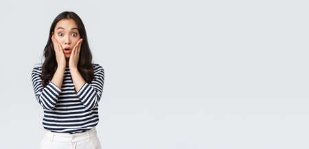 Lifestyle, people emotions and casual concept. Surprised gasping woman stare impressed, losing speech from emotions, drop jaw and touch face amazed, standing white backgroundの写真素材