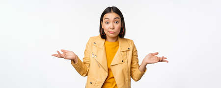 Image of korean girl shrugs shoulders and looks confused, dont know, cant tell, standing over puzzled over white backgroundの写真素材