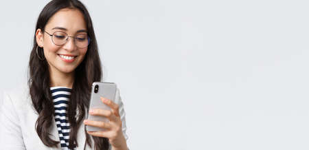 Business, finance and employment, female successful entrepreneurs concept. Close-up of stylish modern businesswoman in suit and glasses messaging, using mobile phoneの写真素材