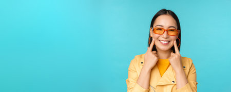Close up portrait of asian young woman in sunglasses, smiling and looking romantic, standing happy...