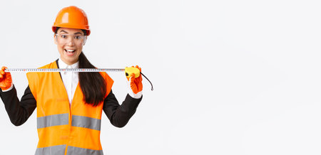 Excited and upbeat asian female construction engineer measuring layout, holding tape measure and...