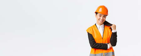 Portrait of confident smiling asian female construction manager, engineer at building area, wearing safety helmet and reflective jacket looking delighted at project, being pleased with finished workの写真素材