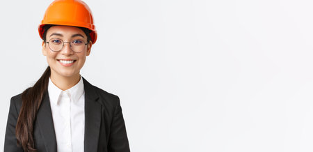Close-up of smiling professional asian female engineer, businesswoman in suit and safety helmet...