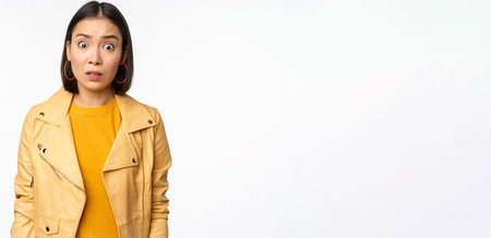 Image of shocked, confused asian woman, staring frustrated and speechless at camera, raising...