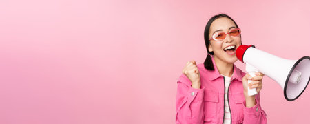 Attention, announcement concept. Enthusiastic asian girl shouting in megaphone, advertising with...
