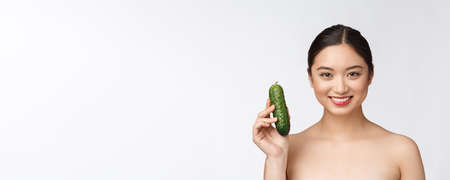 Asian young woman over isolated background holding cucumber.の写真素材