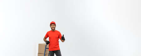 Delivery Concept - Portrait of Handsome African American delivery man or courier pushing hand truck with stack of boxes. Isolated on Grey studio Background. Copy Space.の写真素材