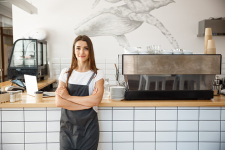 Coffee Business owner Concept - Portrait of happy attractive young beautiful caucasian barista in apron smiling at camera in coffee shop counter.の写真素材