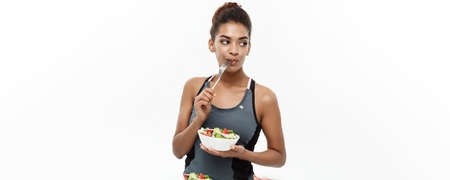 Healthy and Fitness concept - Beautiful American African lady in fitness clothes on diet eating fresh salad. Isolated on white background.の写真素材