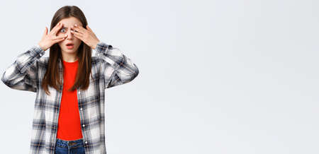 Lifestyle, different emotions, leisure activities concept. Shocked and speechless young pretty female in checked shirt, cover eyes from cringy thing but peeking through fingersの写真素材