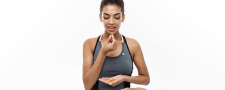 Healthy and Fitness concept - Closeup portrait of beautiful African American taking a pill of Cod liver oil. Isolated on white studio background.の写真素材