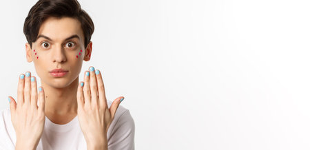 People, lgbtq and beauty concept. Beautiful gay man showing blue nail polish on fingernails and looking at camera, have manicure, standing over white backgroundの写真素材