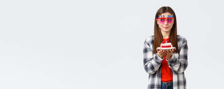 People lifestyle, holidays and celebration, emotions concept. Cute and silly birthday girl in funny glasses, look away think of wish as blowing lit candle on b-day cake, smiling excitedの写真素材