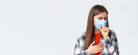 Coronavirus outbreak, leisure on quarantine, social distancing and emotions concept. Close-up of sick young woman in medical mask staying at home during covid-19, cough with closed eyesの写真素材