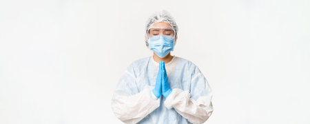 Hopeful asian female doctor or nurse in personal protective equipment and face mask, hoping, praying...