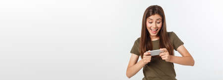 Happy attractive brunette girl joying win in video game on smartphone, isolated over grey backgroundの写真素材