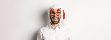 Close-up of excited bearded man in christmas glasses and santa hat looking amazed at promo offer,...