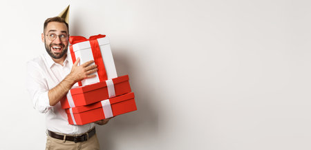 Holidays and celebration. Excited man having birthday party and receiving gifts, looking happy, standing over white backgroundの写真素材
