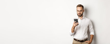 Businessman reading message on phone, standing over white backgroundの写真素材