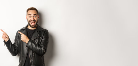 Confident macho man in black leather jacket, pointing fingers left at promo offer, showing logo, white backgroundの写真素材