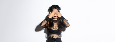 Image of woman wearing gothic wreath and black lace dress shut her eyes with hands, waiting for...