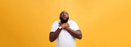 Portrait of african american man with hands raised in shock and disbelief. Isolated over yellow background.の写真素材