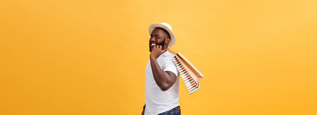 Happy african american man holding shopping bags on yellow background. Holidays conceptの写真素材