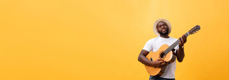 Muscular black man playing guitar, wearing jeans and white tank-top. Isolate over yellow background.